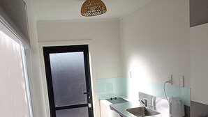 A modern kitchen with a black-framed door, a sink, a kettle, and a small countertop with a magazine. - Opononi Lighthouse Motel (Opononi)