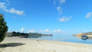 A beach with a sandy shore, a small wooden structure, and a calm body of water. - Opononi Lighthouse Motel (Opononi)