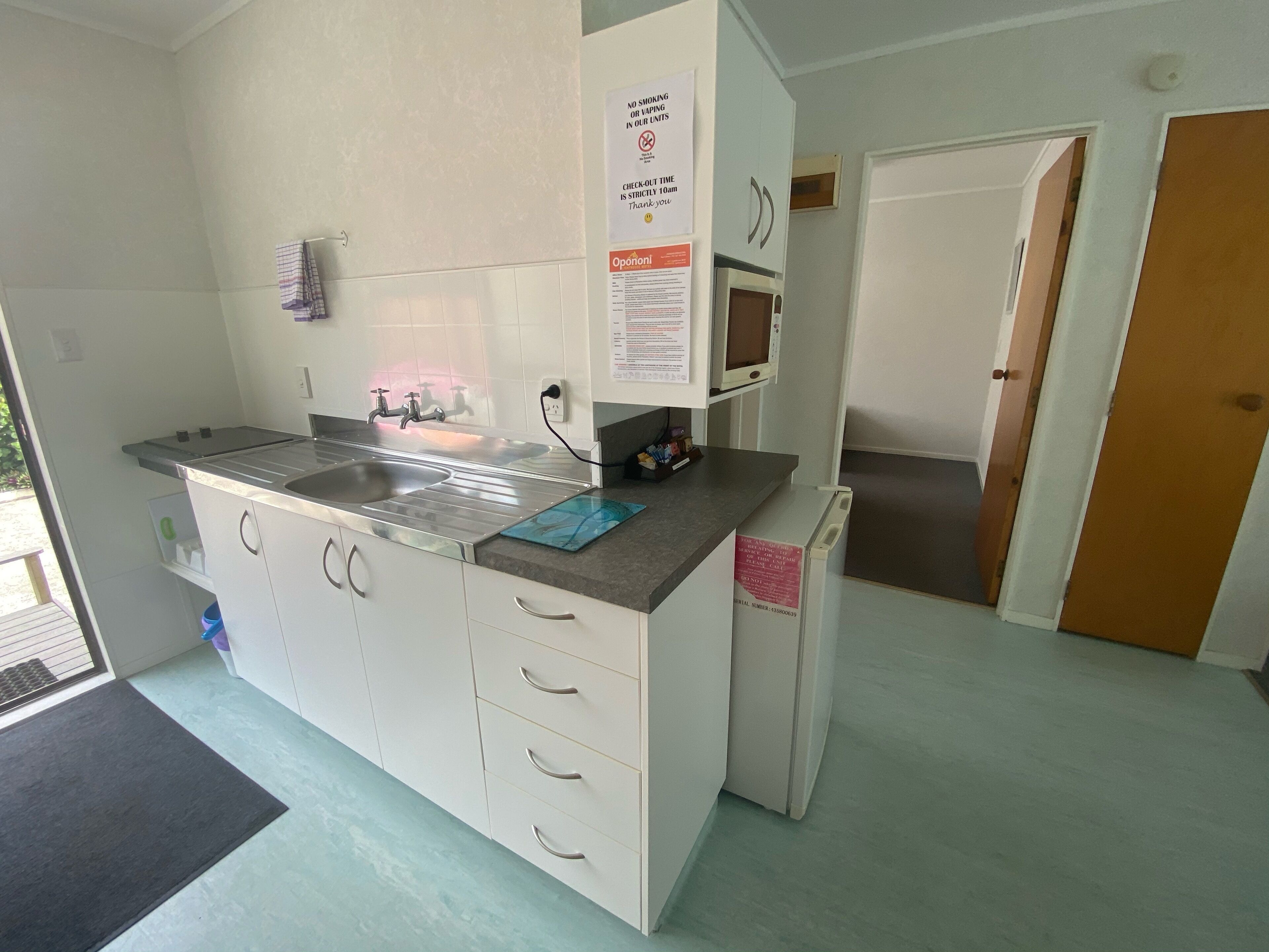 A compact kitchen with a sink, a microwave, and a refrigerator. There is a sign prohibiting smoking and vaping.