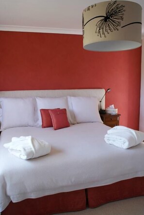 A neatly made bed with white and red pillows, a lamp on a bedside table, and a red wall.