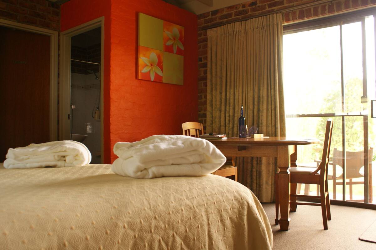 Quarto de hotel com cama, escrivaninha, cadeira e janela com cortinas.