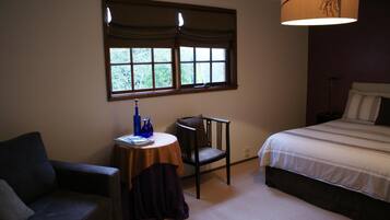A bedroom with a bed, a chair, a small table with a lamp, and a window with curtains.