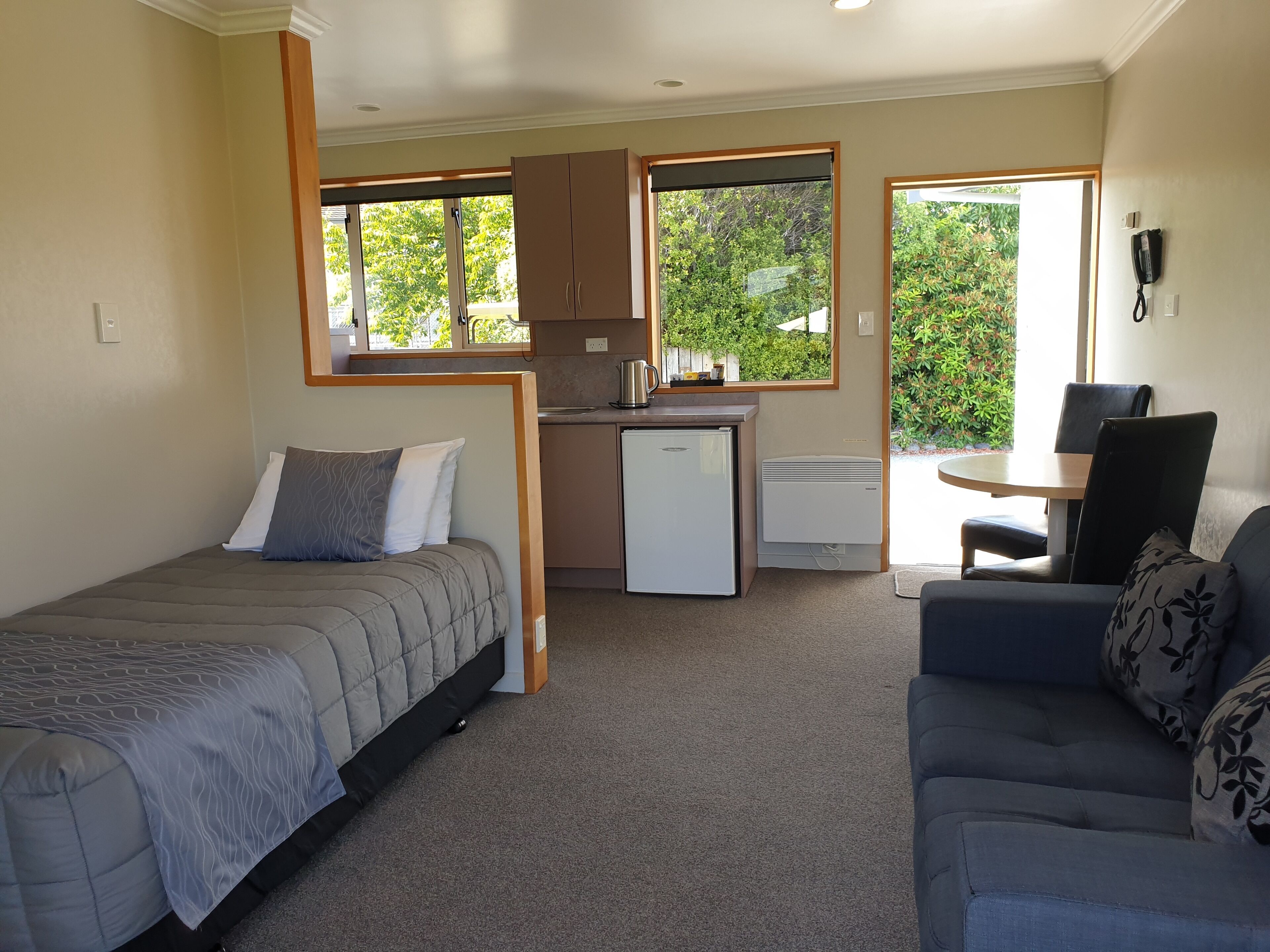 A compact room with a bed, a sofa, a kitchenette, and a dining area.