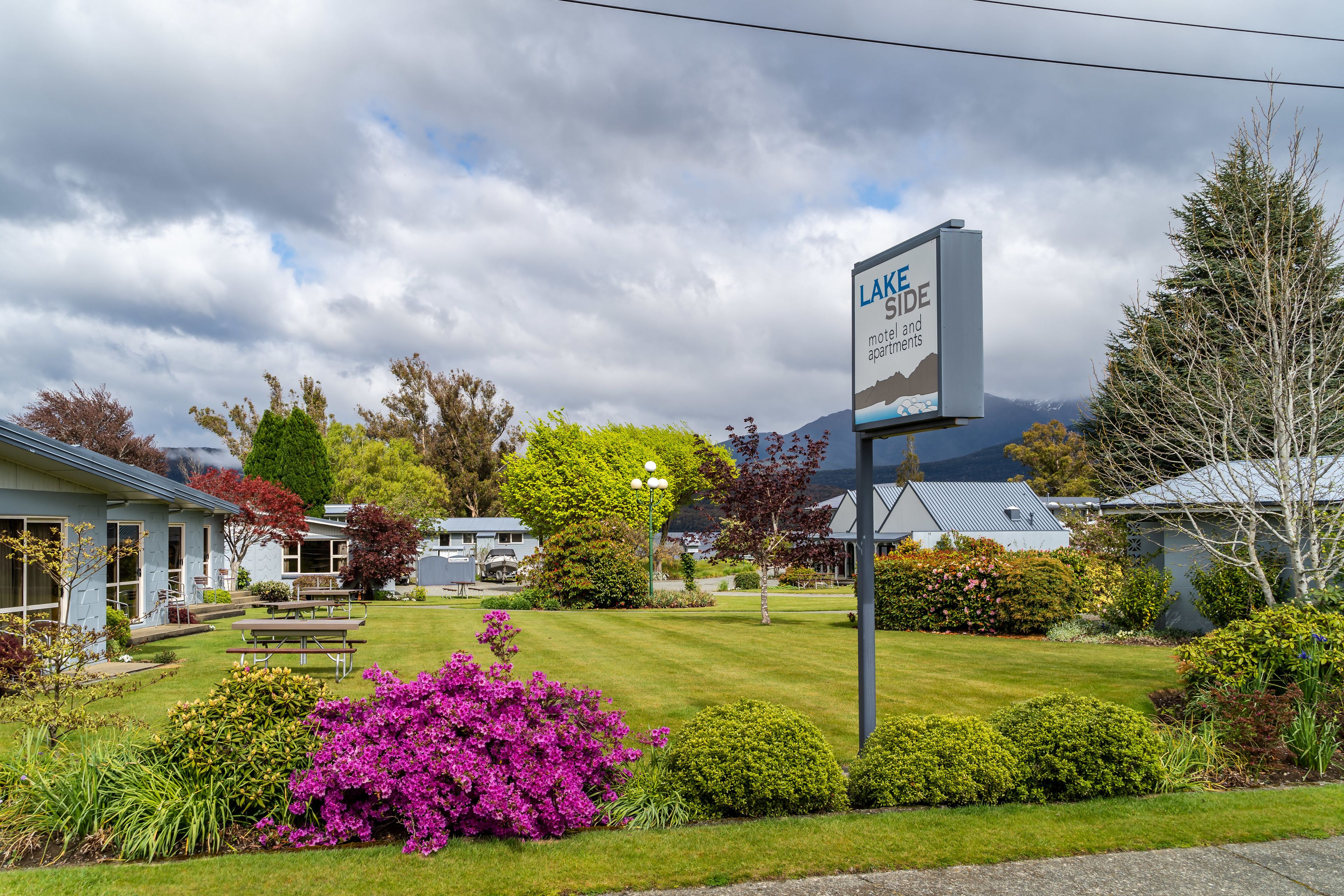 A motel sign with a mountain view, surrounded by well-maintained lawns and various shrubs.