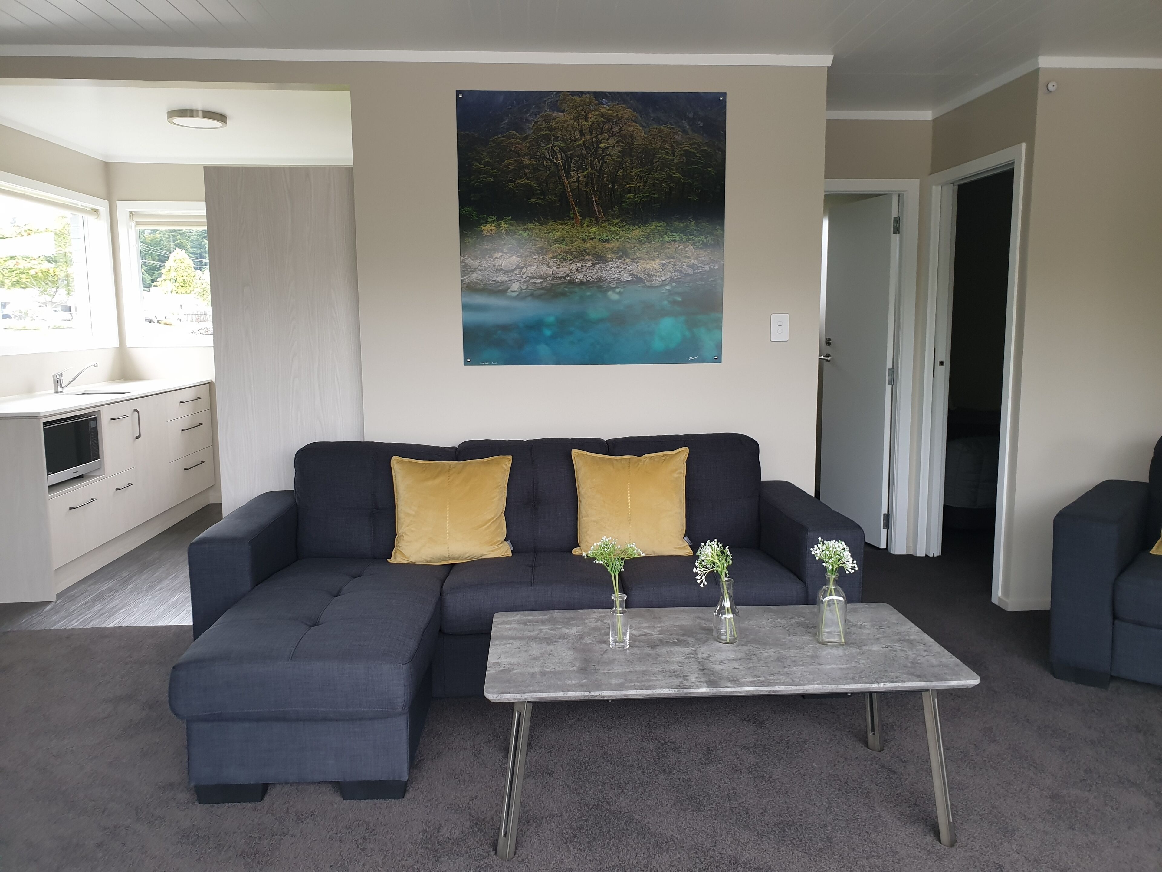 A modern living room with a sectional sofa, a coffee table, and a painting of a natural landscape.