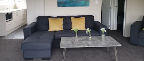 A modern living room with a sectional sofa, a coffee table, and a painting of a natural landscape.