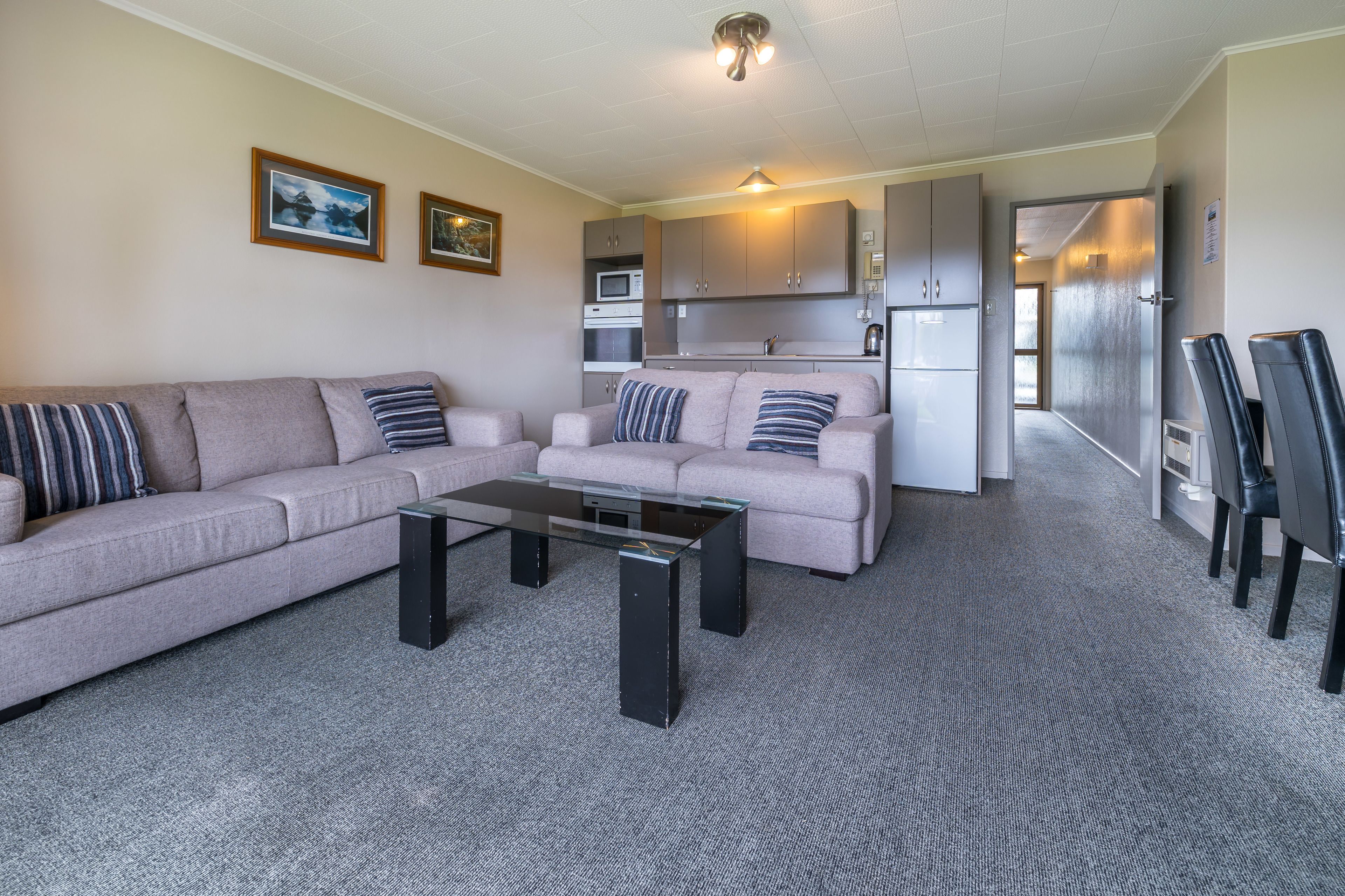 A living room with a sofa, a coffee table, and a kitchenette in the background.