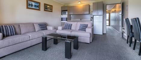 A living room with a sofa, a coffee table, and a kitchenette in the background.