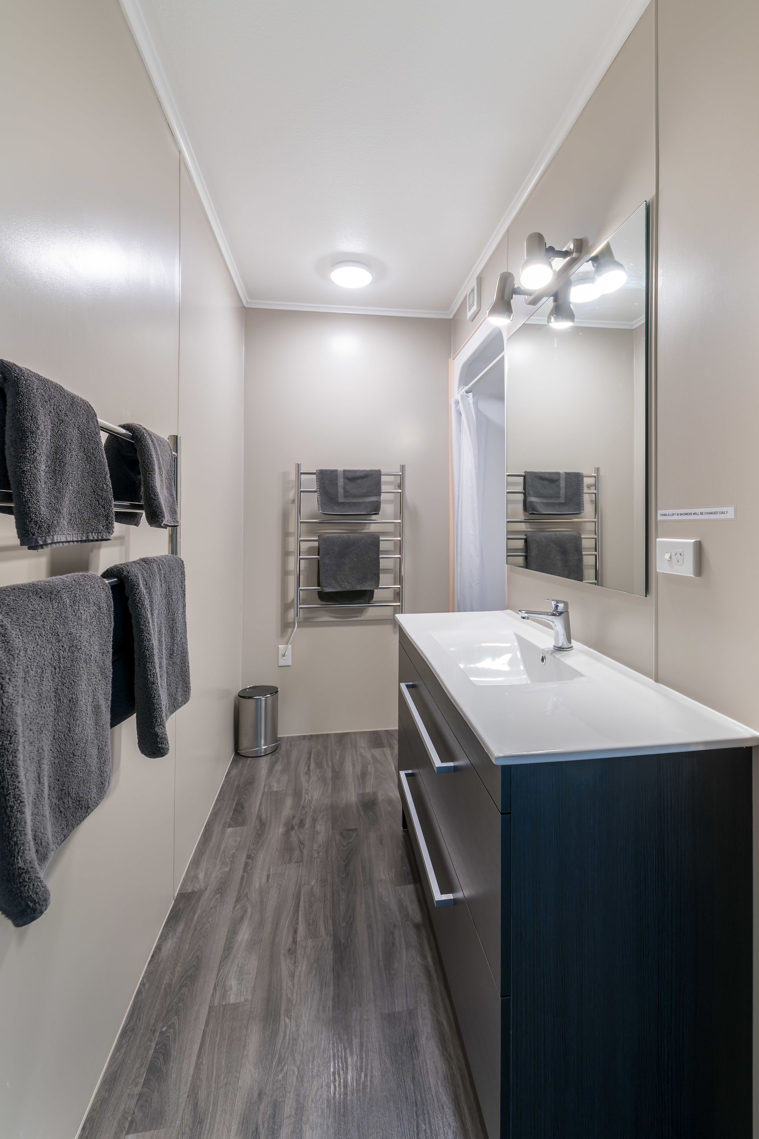 A modern bathroom with a white sink, dark wood flooring, and grey towels on a rack.