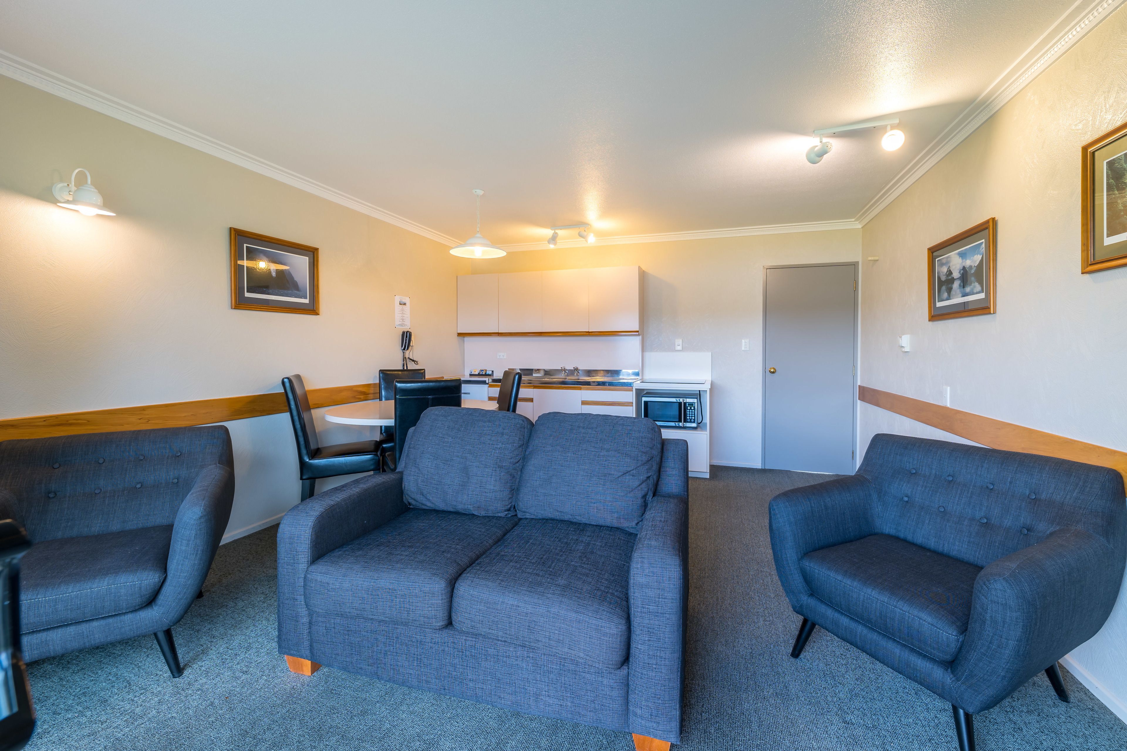 A room with a grey sofa, two armchairs, a dining table with chairs, a microwave, and a refrigerator.