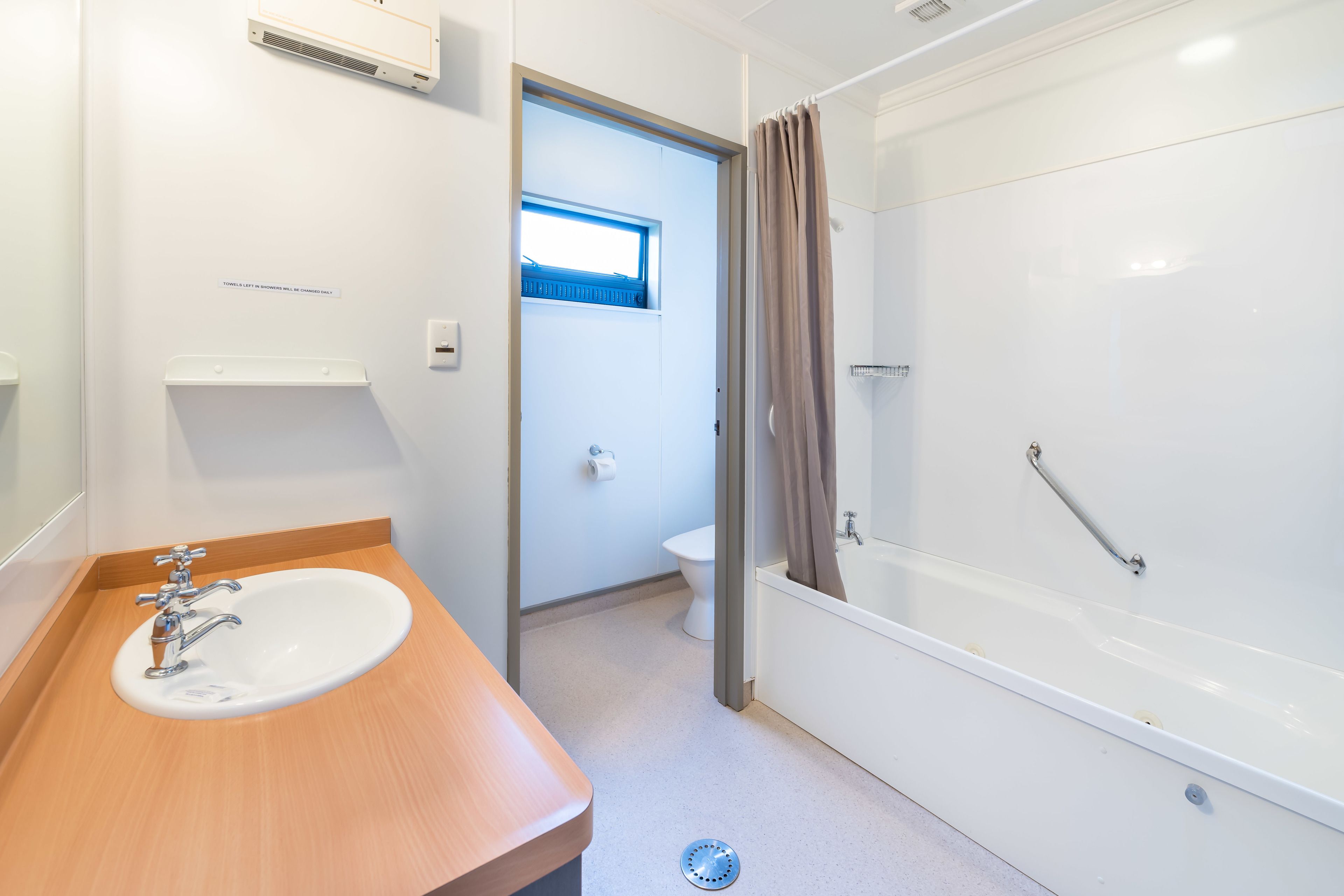 A modern bathroom with a wooden vanity, a white sink, a bathtub, and a toilet.