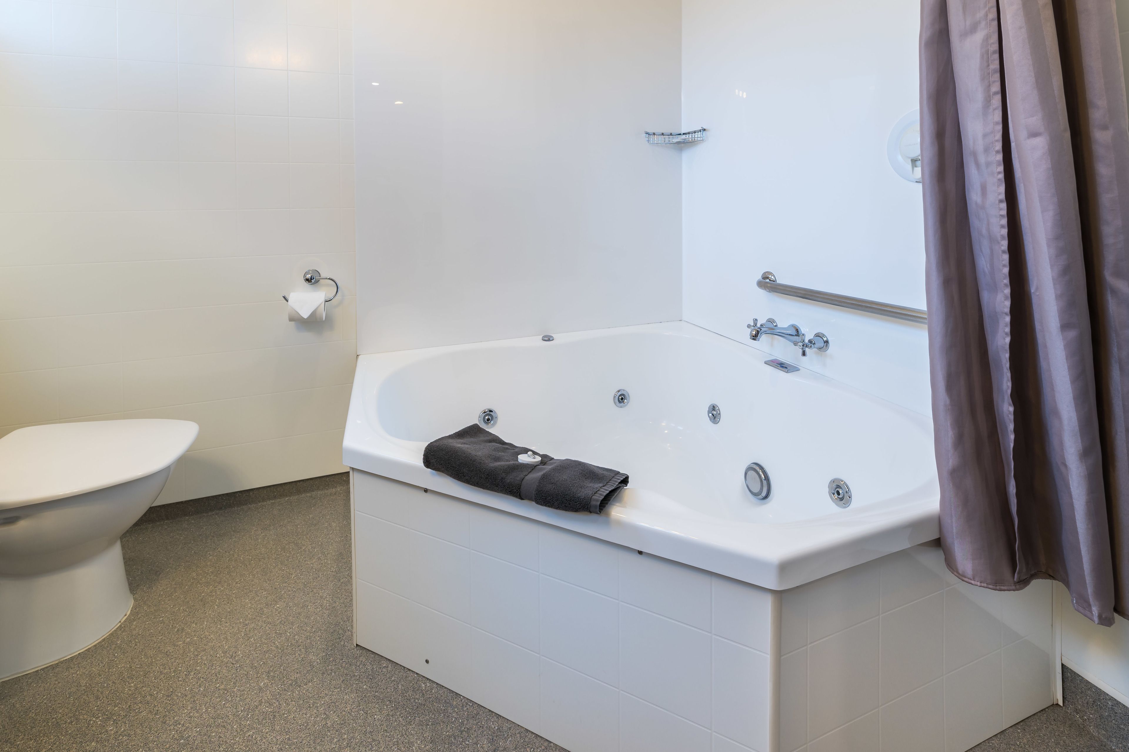 A modern bathroom with a white bathtub, a toilet, and a shower curtain.