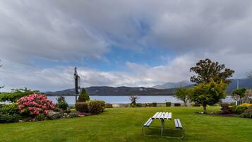 A grassy area with a picnic table and a lamppost, overlooking a lake with mountains in the background.