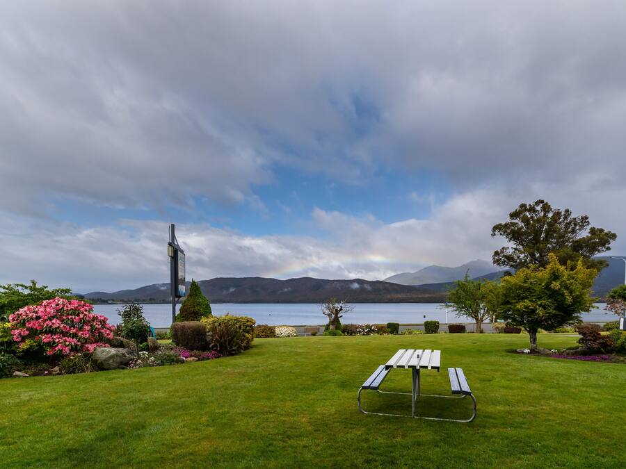 A grassy area with a picnic table and a lamppost, overlooking a lake with mountains in the background.