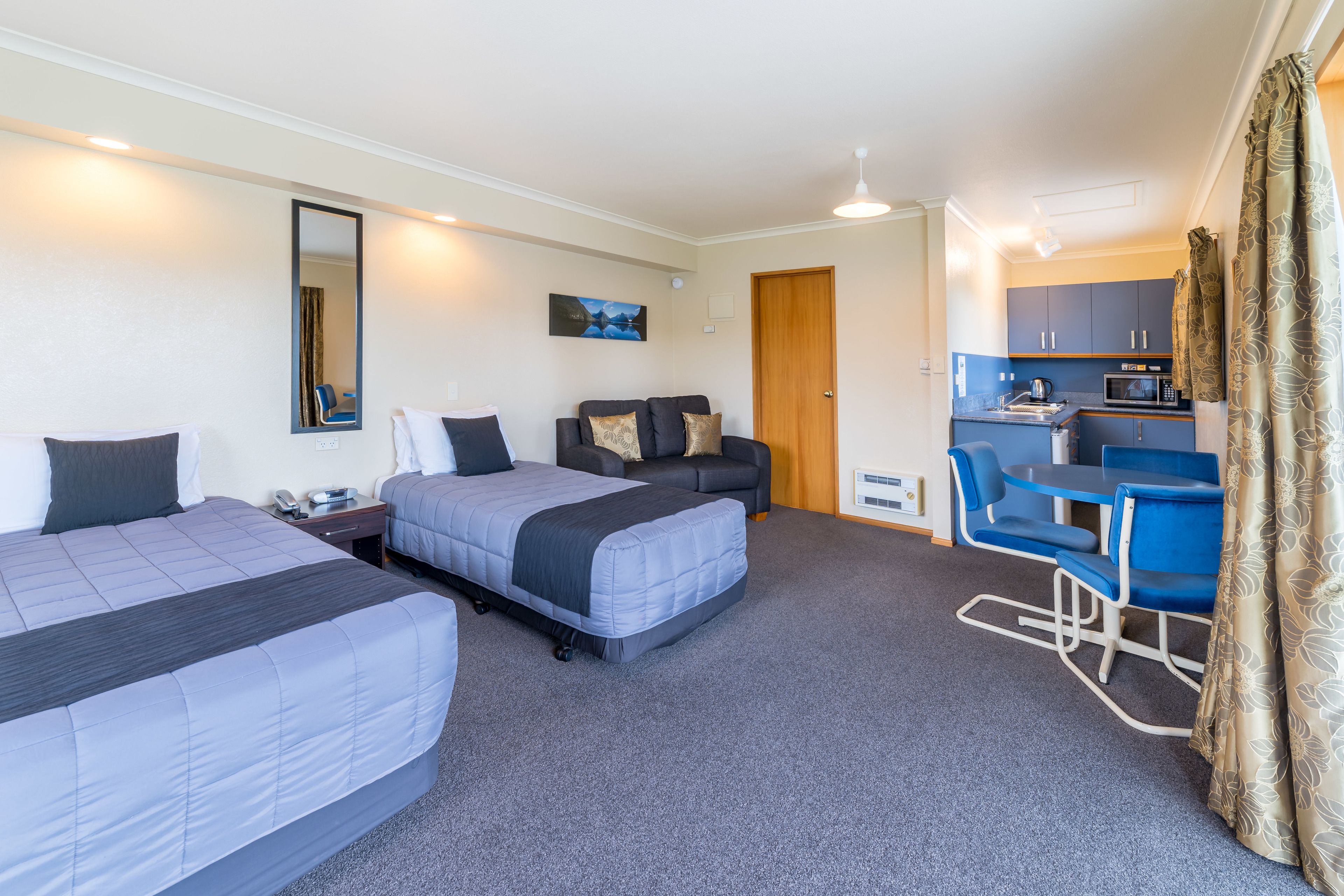 A hotel room with two beds, a desk, a chair, a small kitchenette, and a bathroom.
