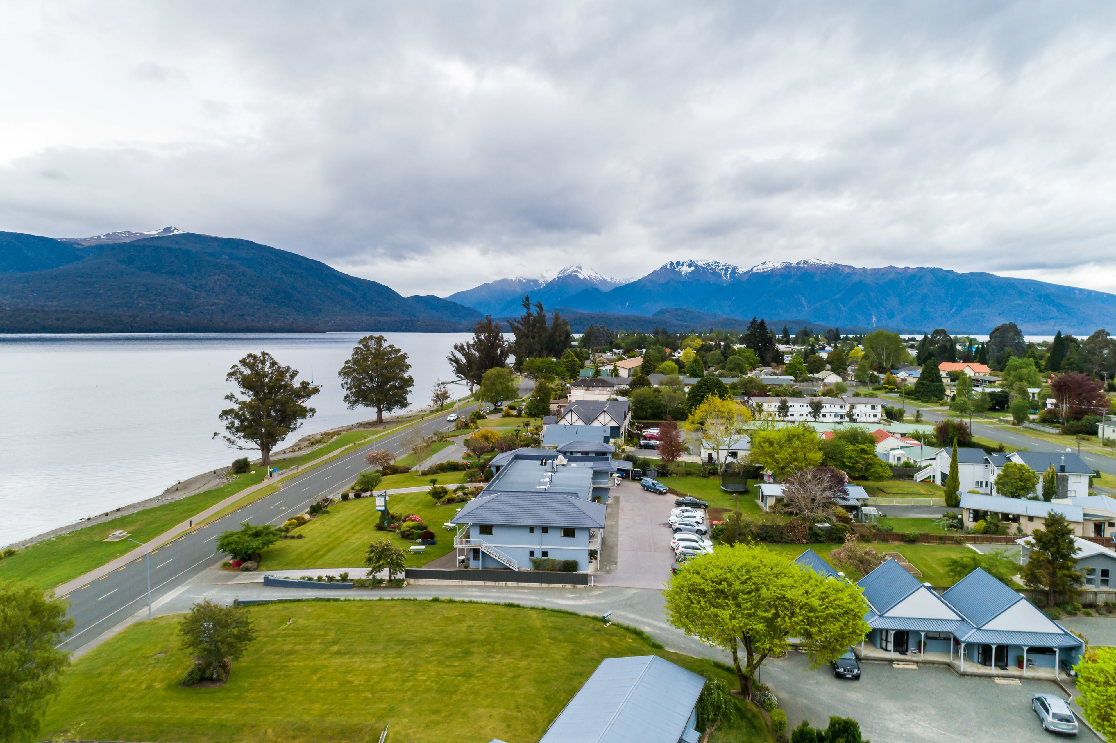 A residential area with houses, a road, and a lake with mountains in the background.