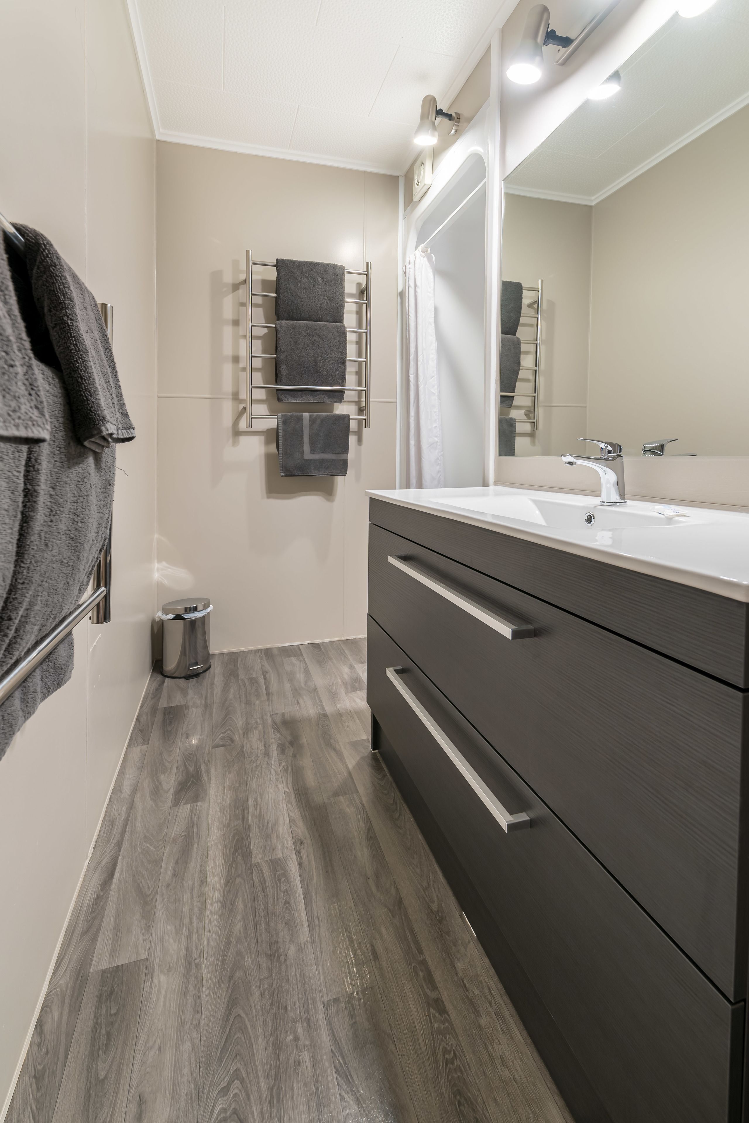 Un baño moderno con un espejo grande, tocador de madera oscura y un perchero con varias toallas.