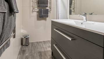 Un baño moderno con un espejo grande, tocador de madera oscura y un perchero con varias toallas.