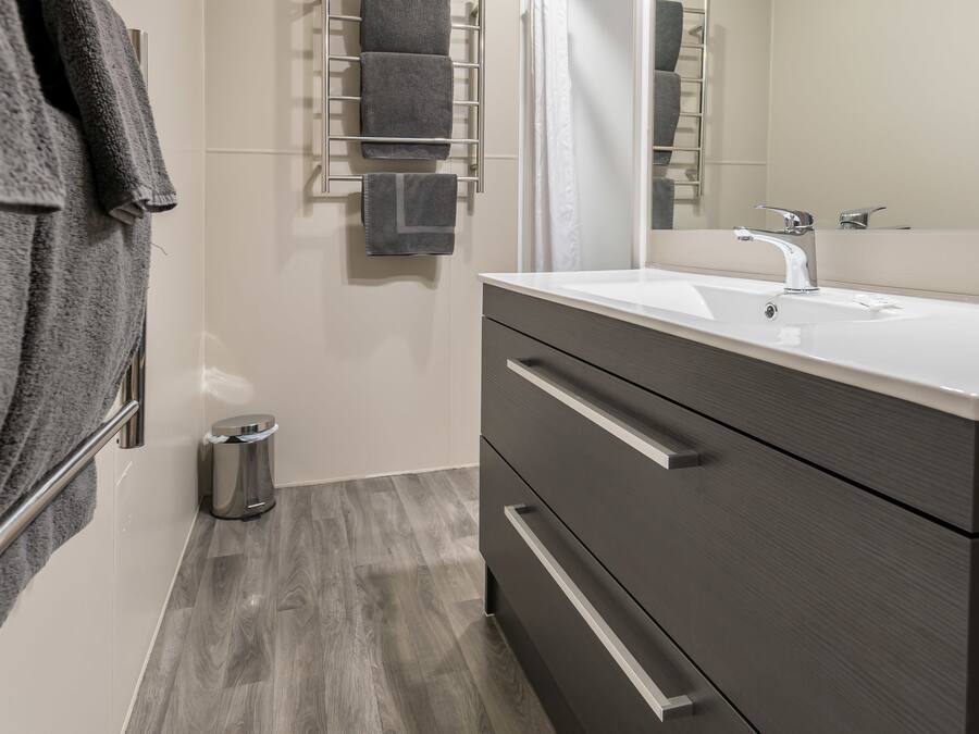 Un baño moderno con un espejo grande, tocador de madera oscura y un perchero con varias toallas.