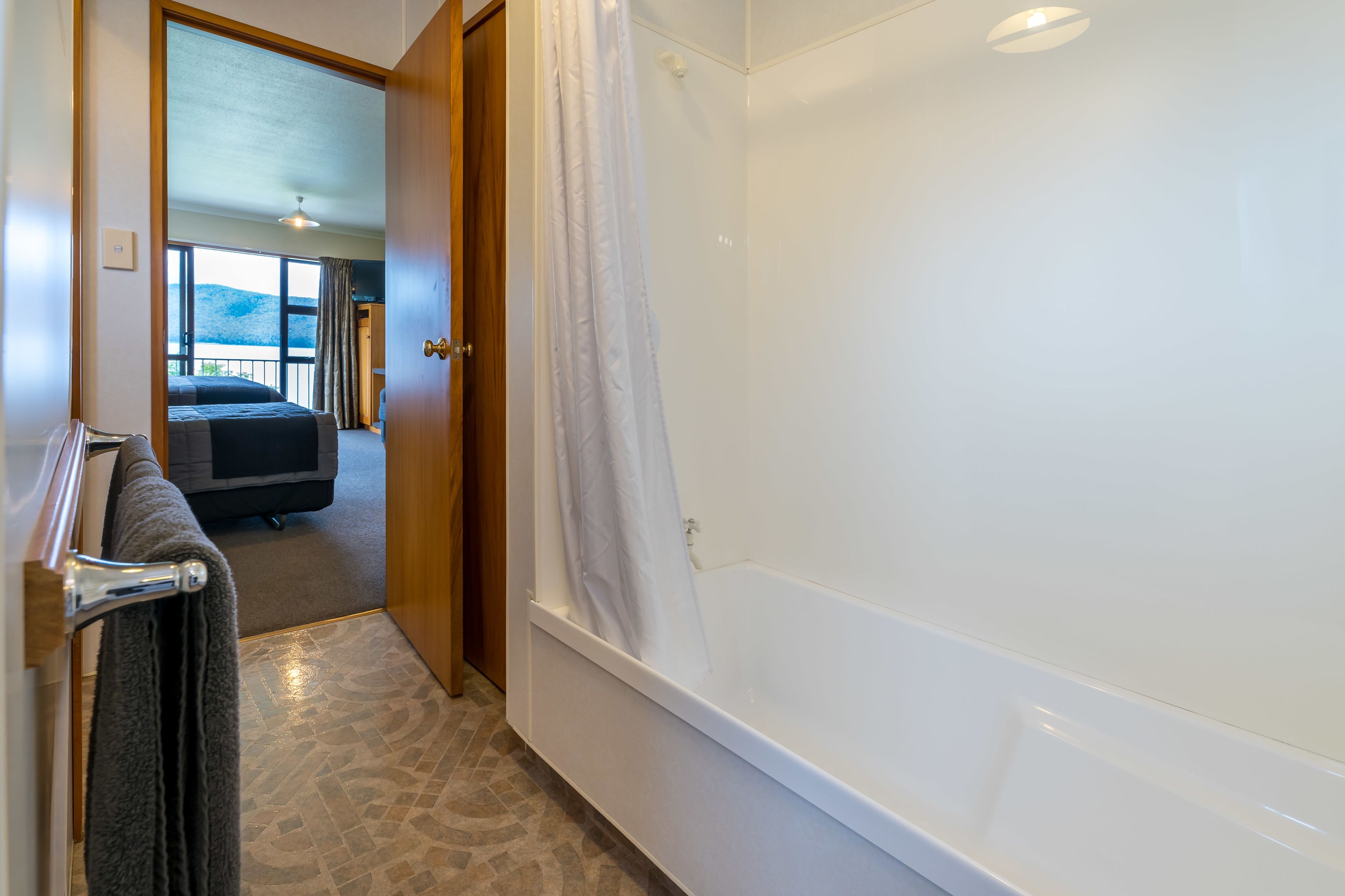 A bathroom with a bathtub, a towel rack, and a view of a balcony with a bed.
