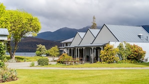 A building with a white exterior and a metal roof, surrounded by a well-maintained lawn and various shrubs. - Lakeside Motel & Apartments (Te Anau)