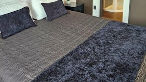 A bedroom with a large bed, a nightstand, a potted plant, and a shower area. - Lakeside Motel & Apartments (Te Anau)