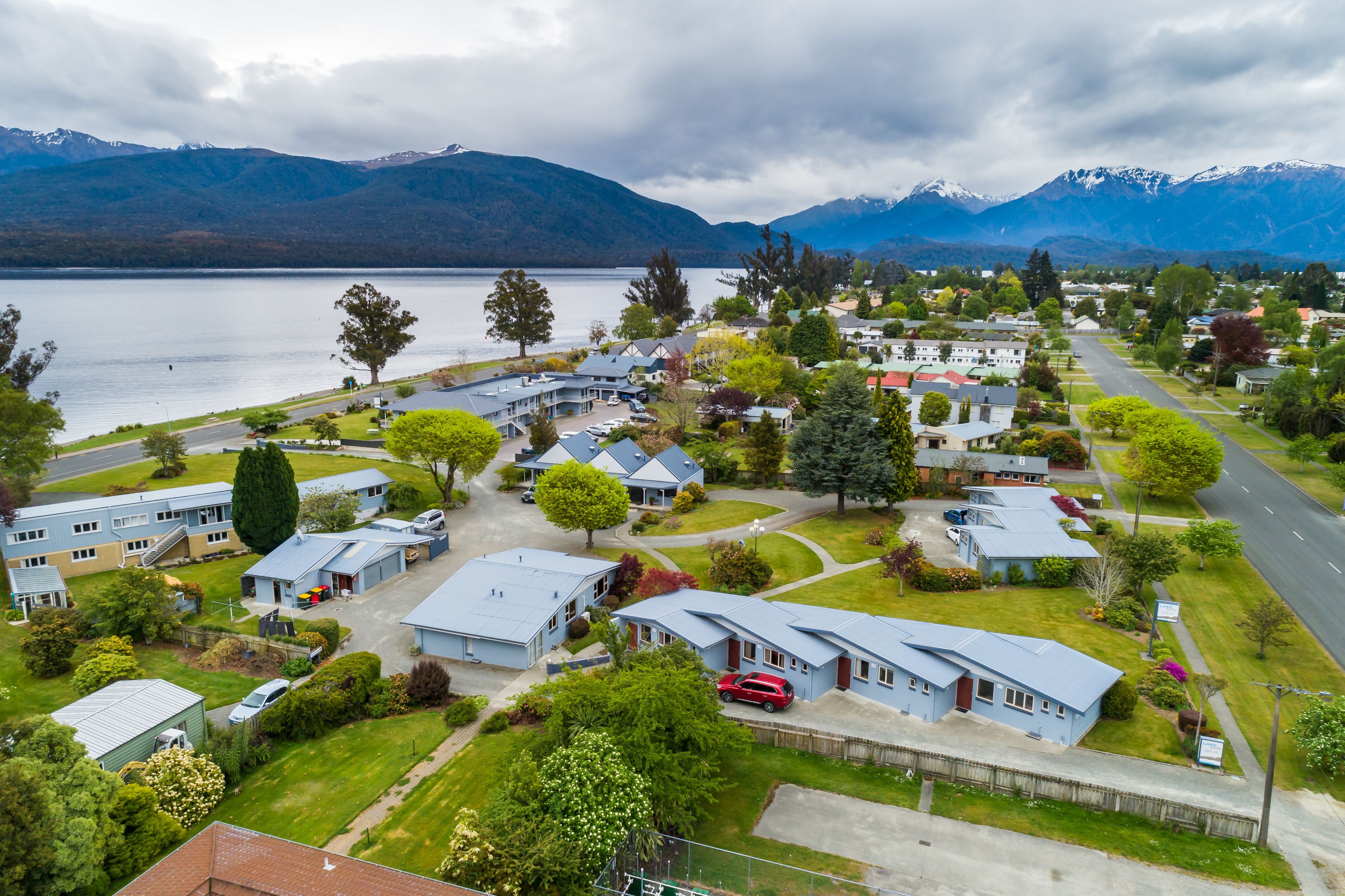 A residential area with houses, a road, and a lake with mountains in the background.