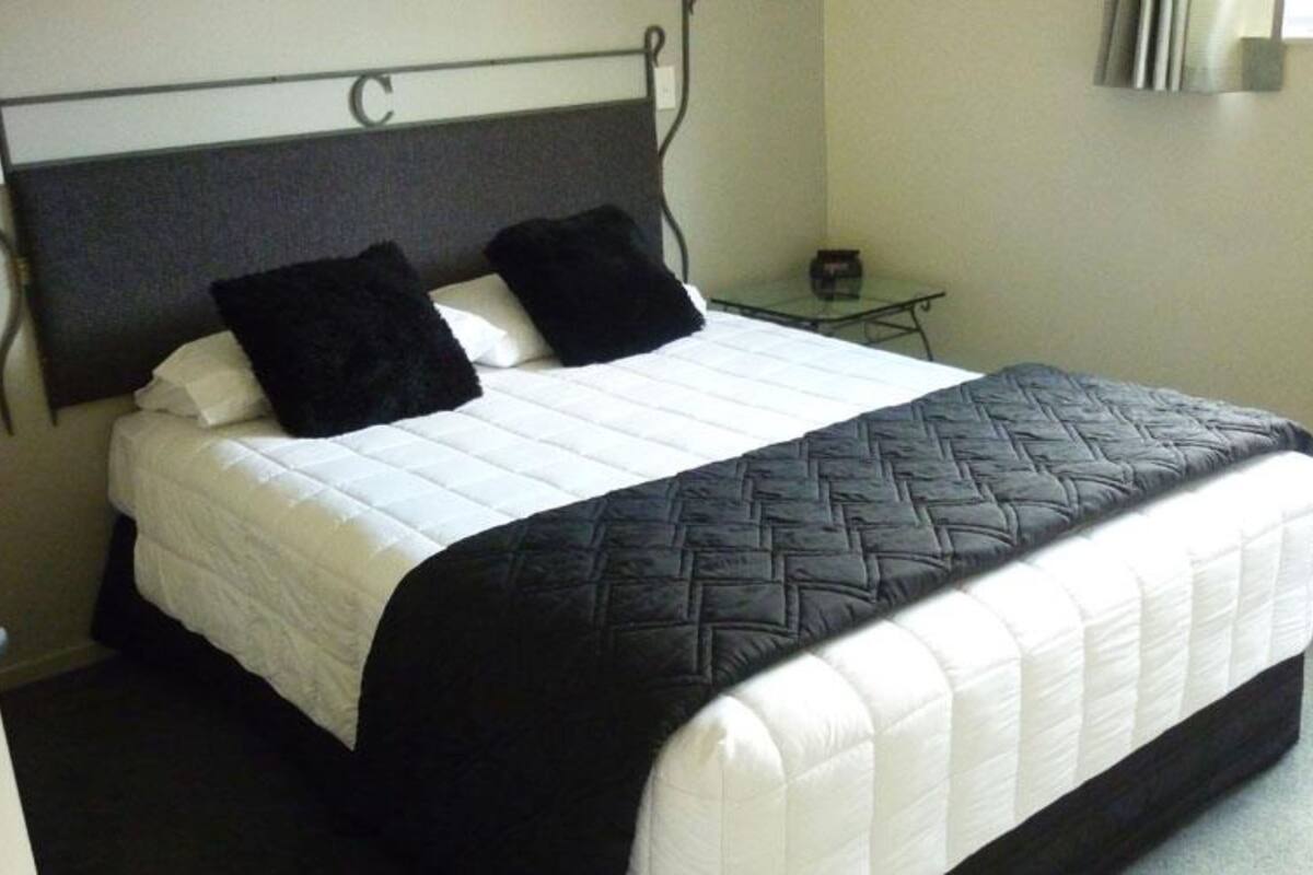 A neatly made bed with a black and white quilt, a metal headboard, and a small bedside table with a lamp.