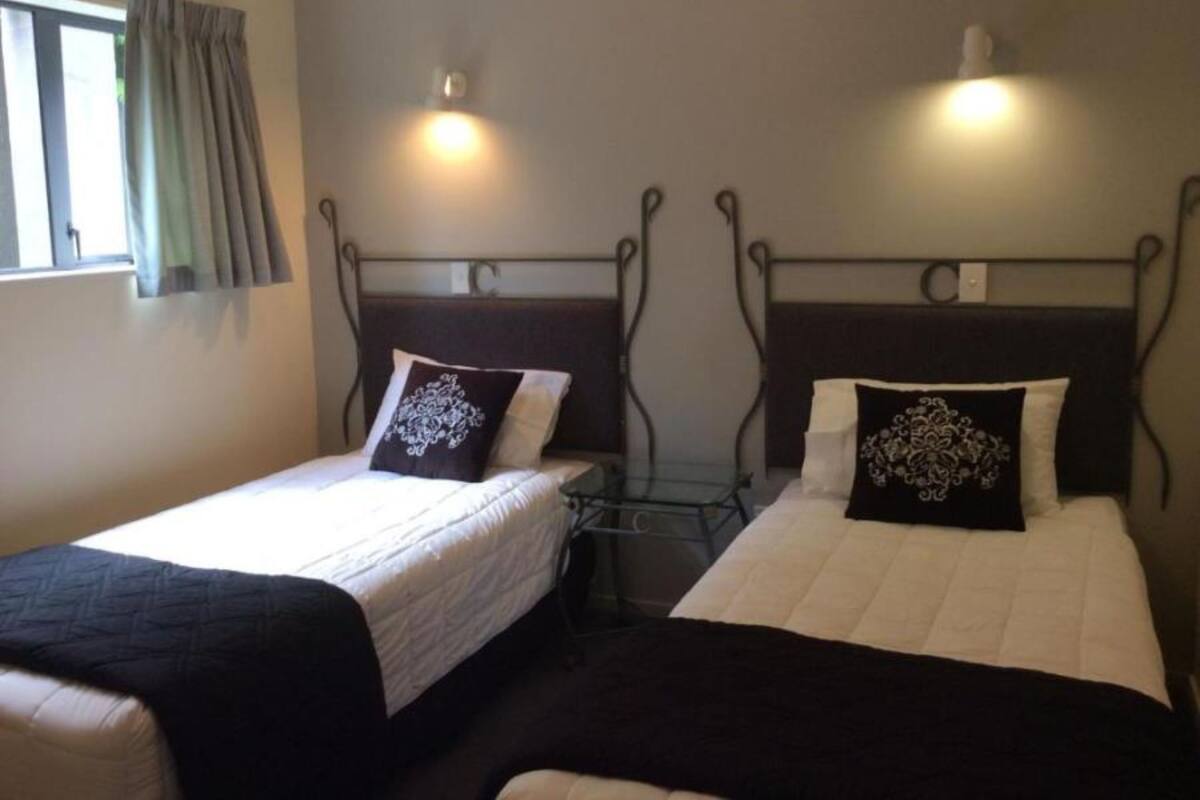 Two single beds with metal headboards, a window with curtains, and a wall-mounted light fixture.