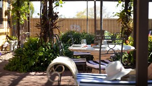 A garden patio with a round table set for two, surrounded by lush greenery and a wooden pergola. - The Table Guesthouse (Greta)
