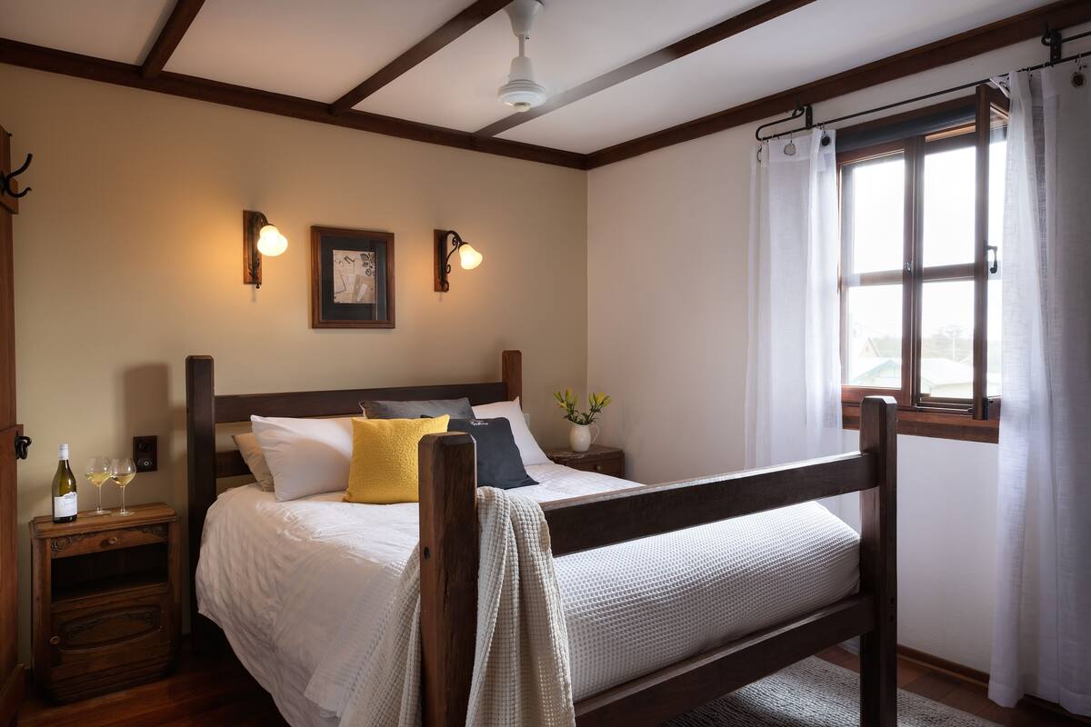 Une chambre à coucher avec un lit en bois, une literie blanche, une table de chevet avec une bouteille et des verres, et des lampes fixées au mur.