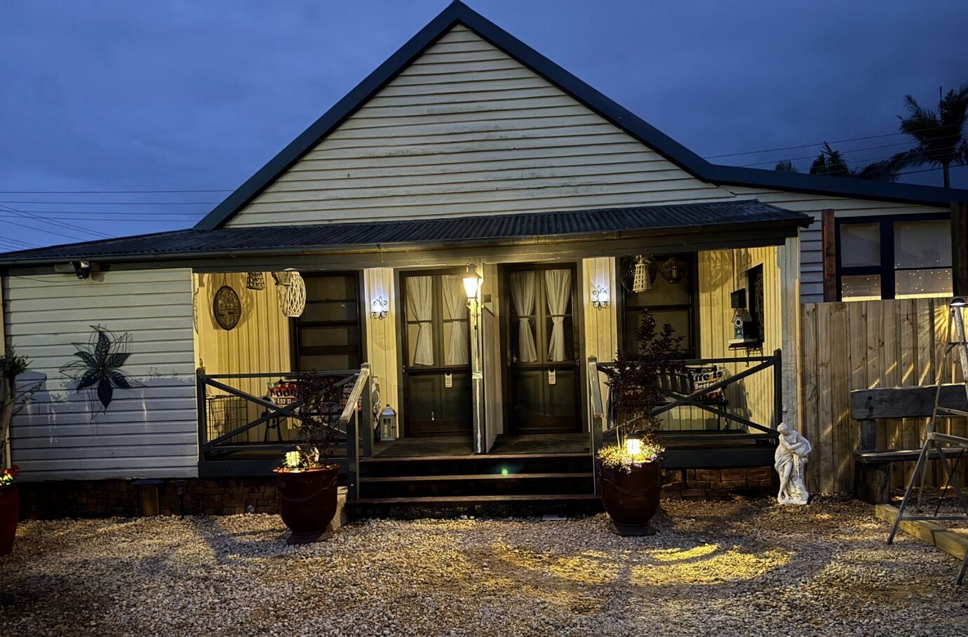 A single-story building with a gabled roof, a front porch with a bench, and two potted plants.