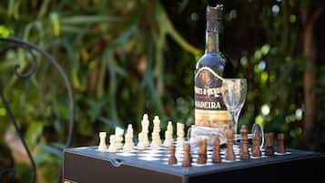 A chessboard with pieces, a bottle, and a glass on a table outdoors.
