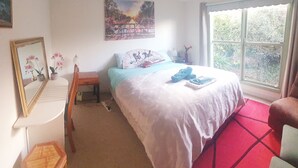 A bedroom with a bed, a chair, a window, a mirror, and a painting on the wall.