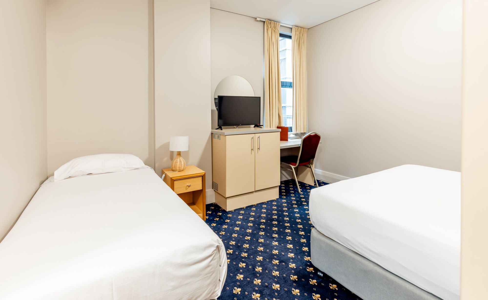 Una habitación de hotel con dos camas, un escritorio, un televisor, una lámpara y una silla.