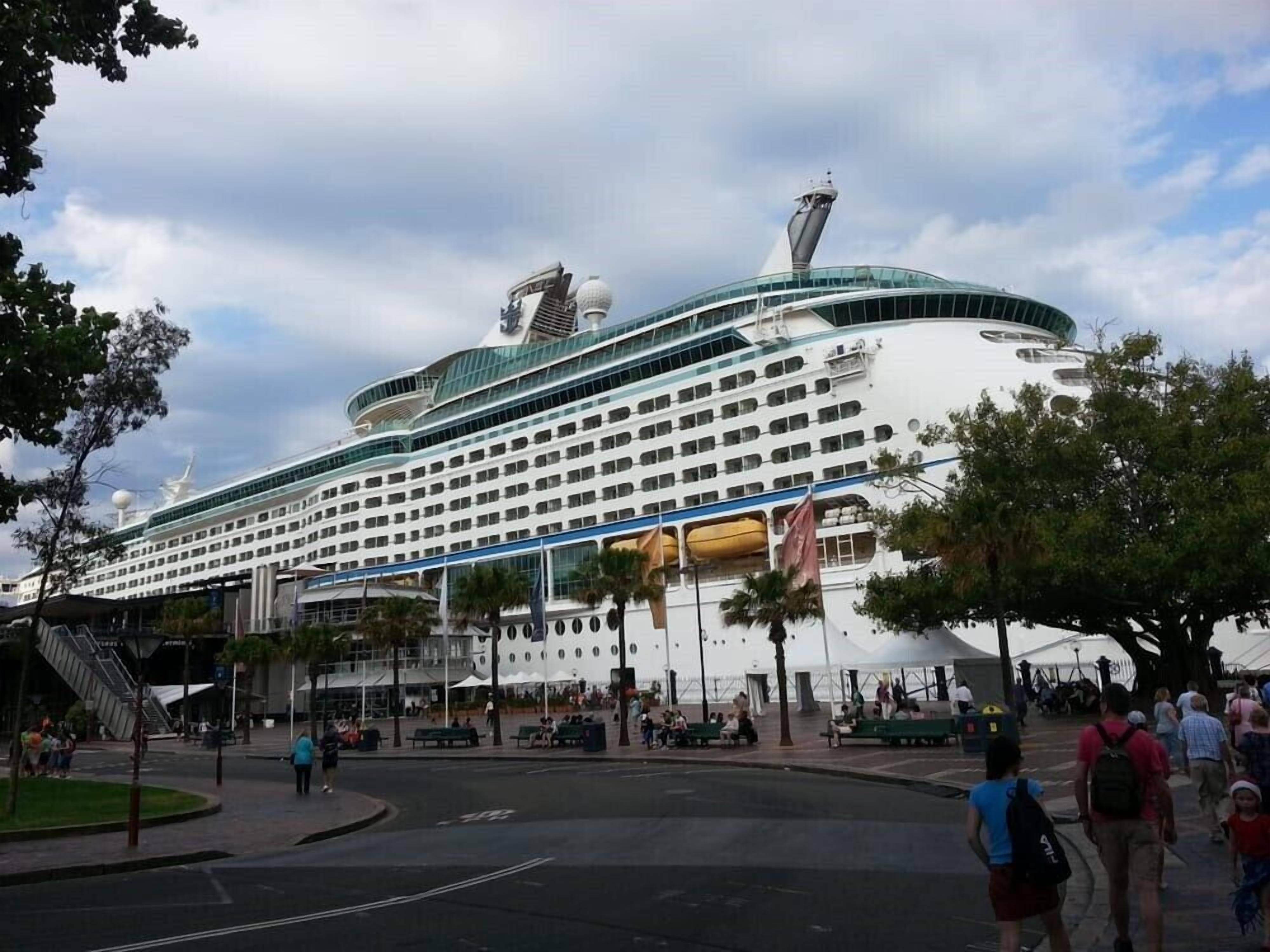 Un gran crucero amarrado en un puerto, con un edificio terminal al frente.