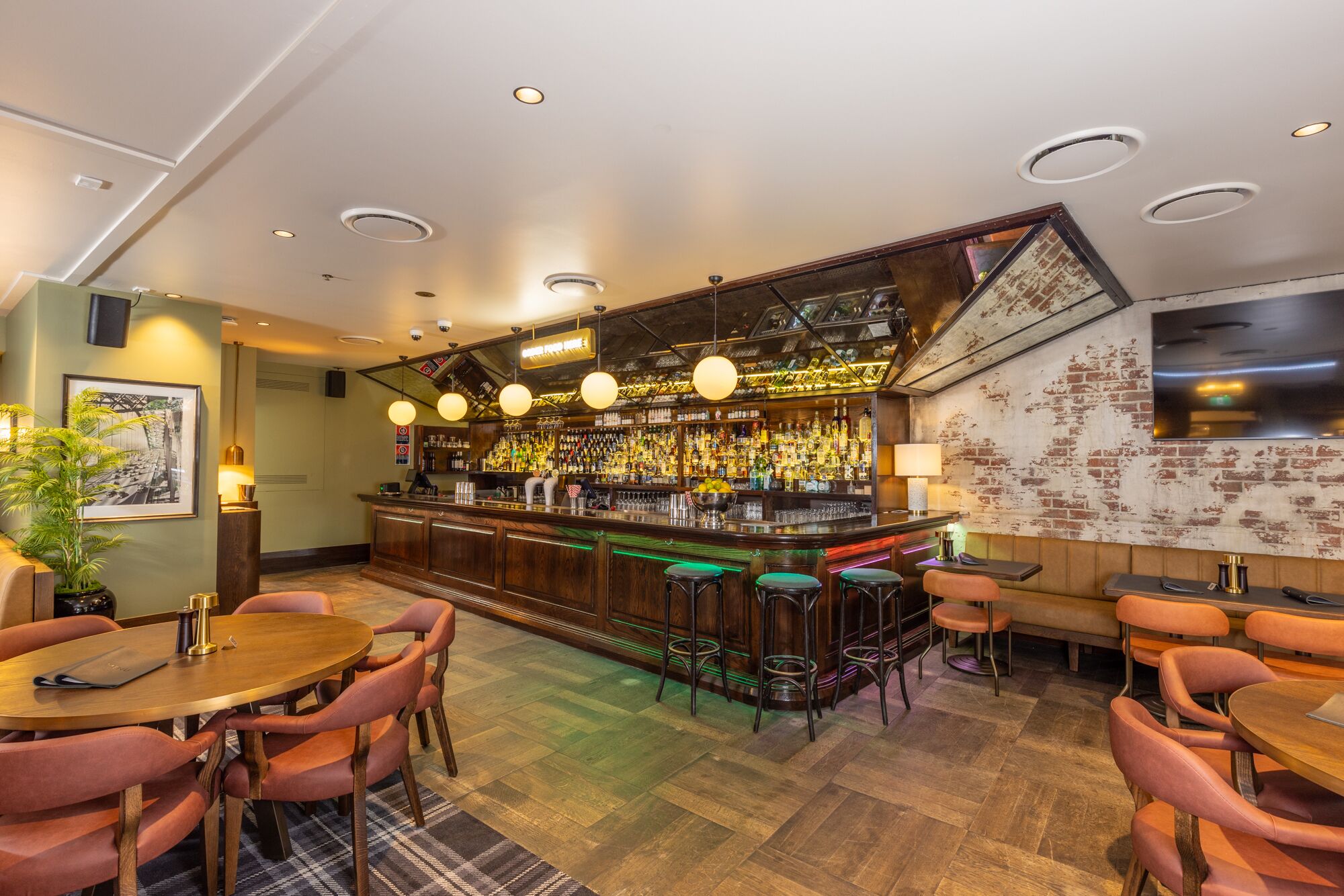 A bar area with a wooden bar counter, multiple stools, and a seating area with tables and chairs.