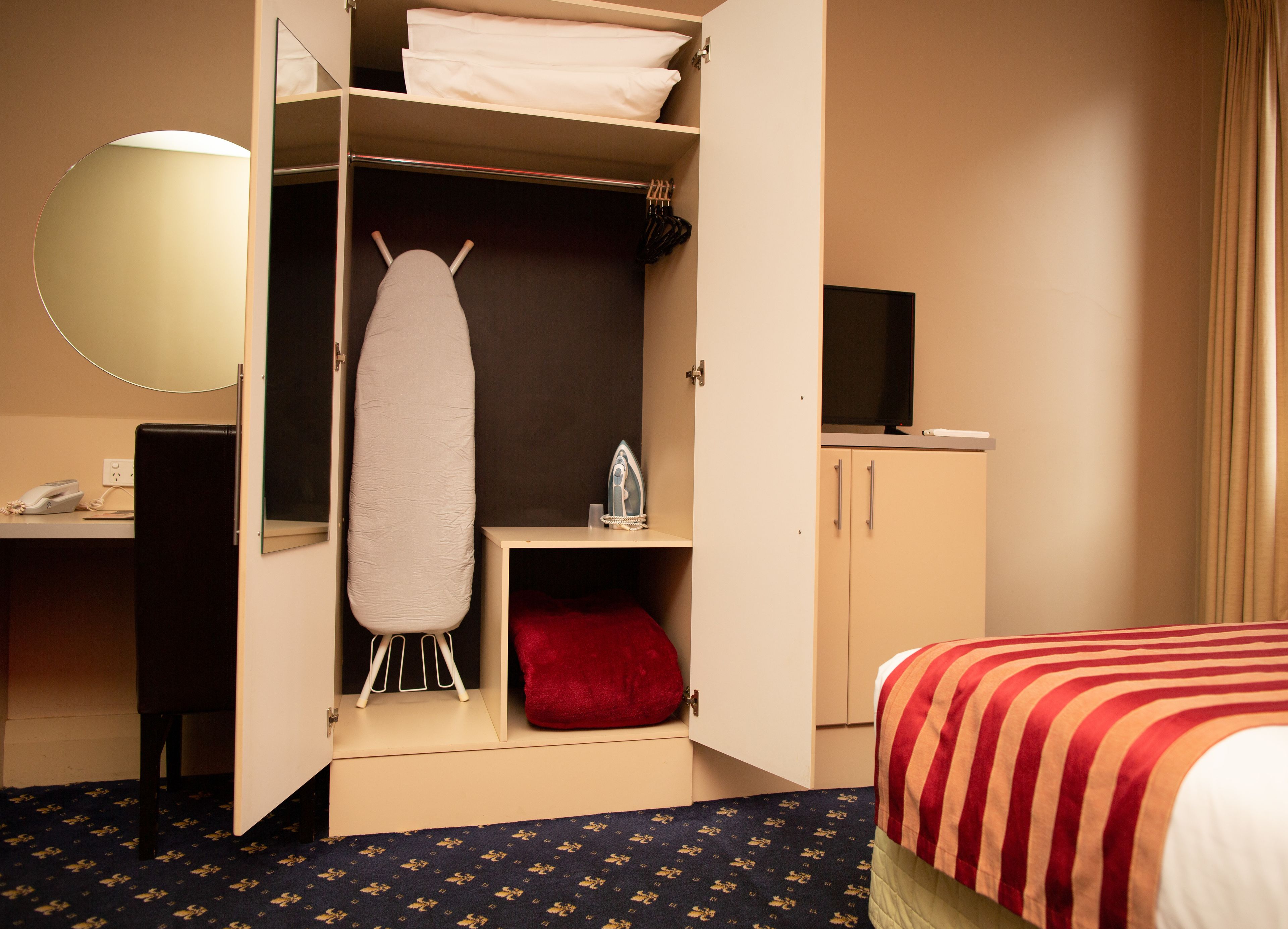 Een hotelkamer met een bed, een bureau, een kledingkast en een strijkplank.