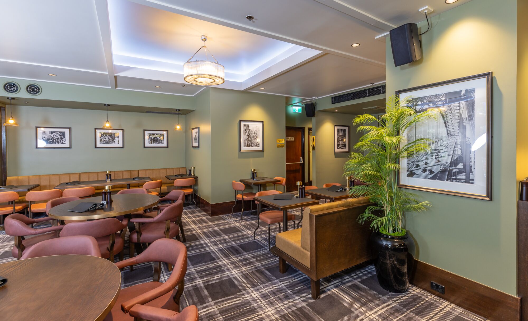 Een restaurant met zitjes, ronde tafels en een grote kamerplant.