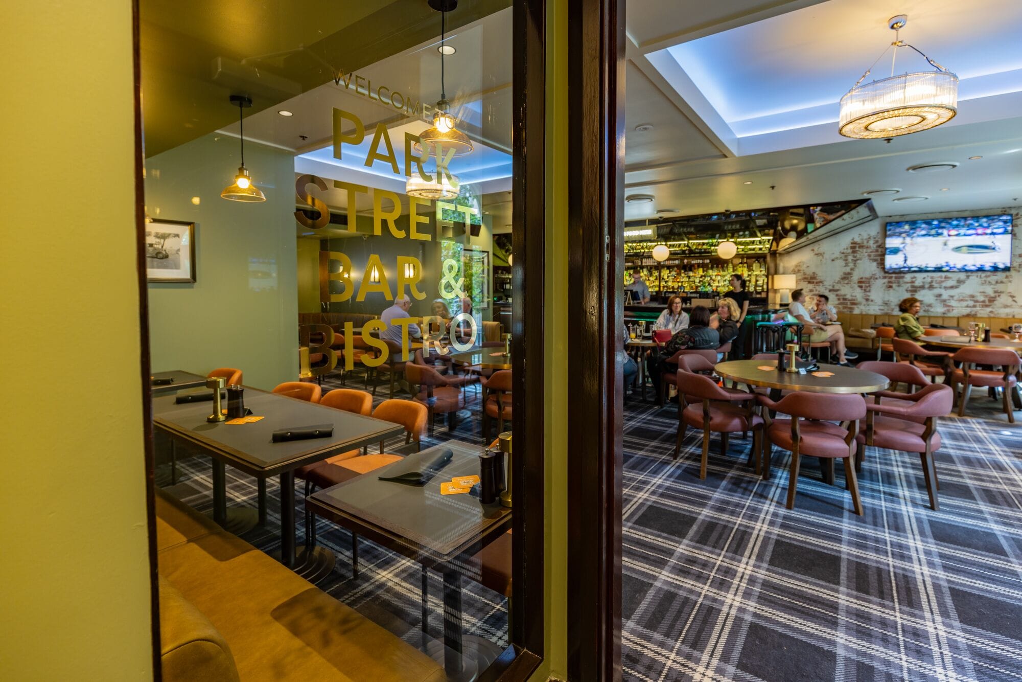 A restaurant with a bar and a coffee shop, featuring a plaid carpet and wooden tables.