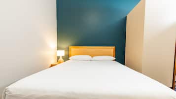 Een netjes opgemaakt bed met witte lakens in een kamer met een blauwe accentmuur en een houten hoofdbord.