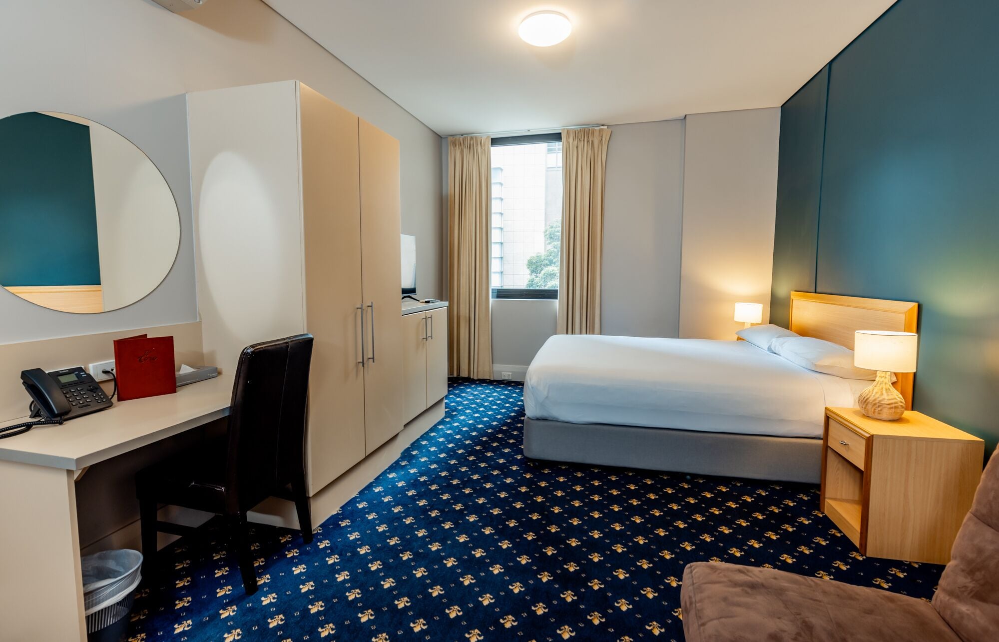 Una habitación de hotel con cama, escritorio, silla y una mesita con lámpara.