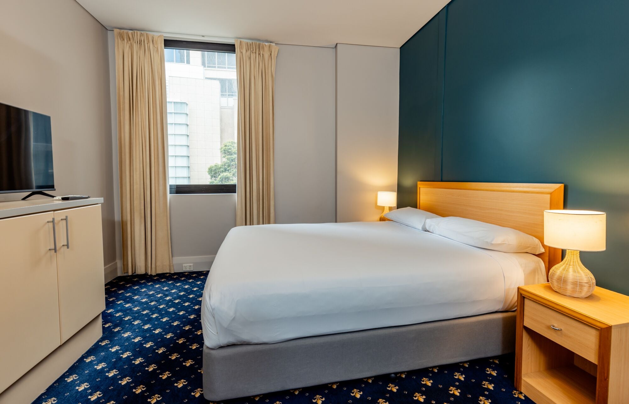 Une chambre d’hôtel avec un lit, des lampes de chevet, une télévision et une fenêtre avec des rideaux.