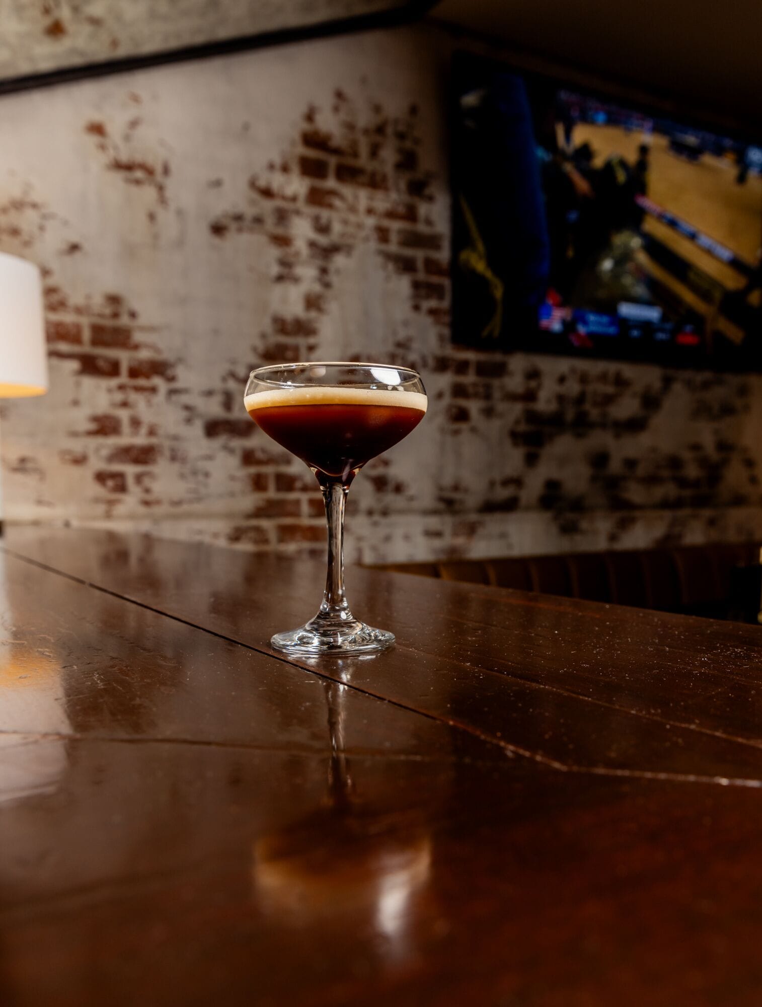 A martini glass with a dark liquid on a bar counter.