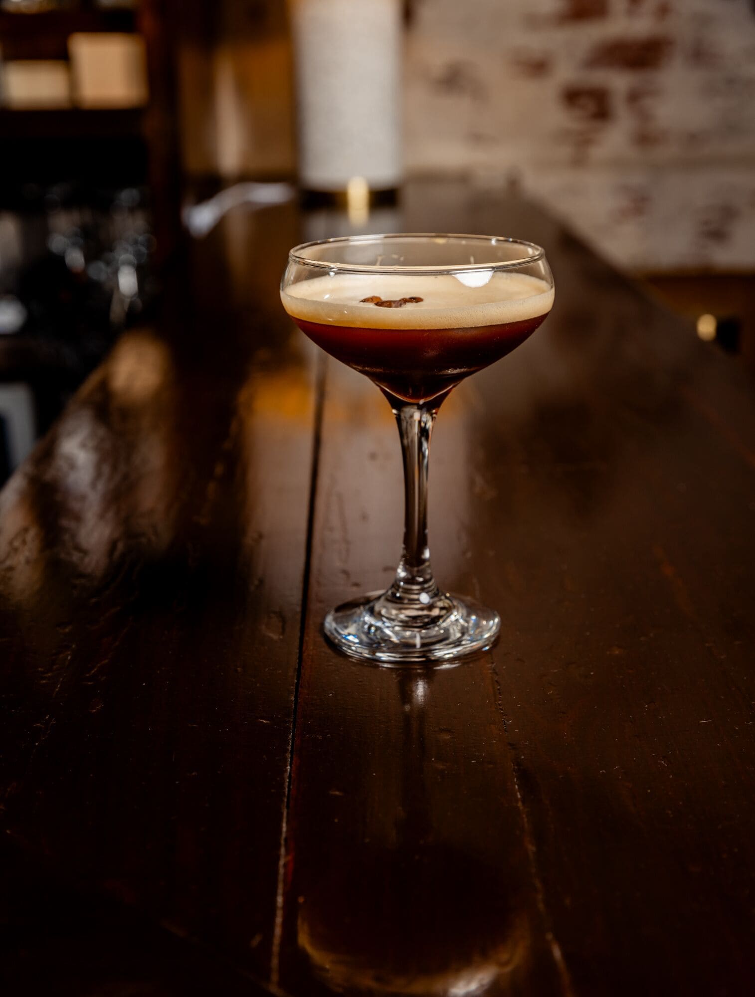 A martini glass with a foamy head on a wooden bar counter.