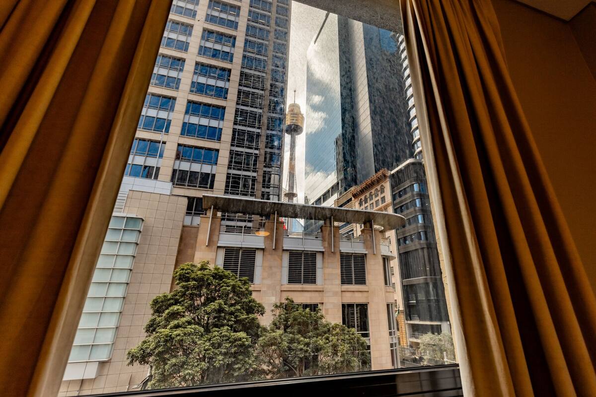 A view from inside a room with a large window overlooking a modern building with multiple floors and a mix of architectural styles.