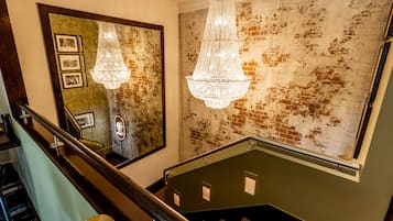 Una escalera con barandilla de madera, un candelabro y una pared con ladrillo desgastado.
