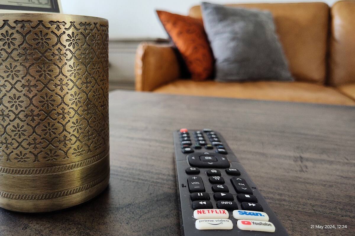 A remote control with buttons for Netflix, Prime Video, Stan, and YouTube, and a decorative vase on a table.