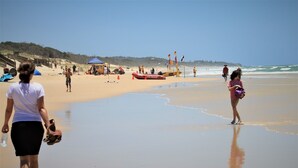 A beach with people walking, a surf rescue boat, and lifeguard flags.