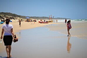 A beach with people walking, a surf rescue boat, and lifeguard flags.